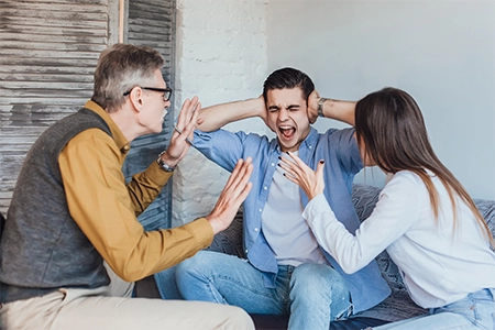 jovem gritando e tapando os ouvidos enquanto seus pais tentam falar com ele