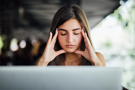 jovem estressada, com as mãos no rosto, de frente para um monitor